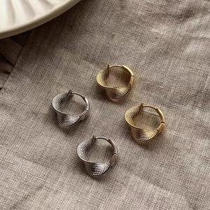 Macro detail of twisted Mobius earrings in gold and silver with textured finish on linen