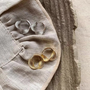 Detail of gold and silver twisted hoop earrings with textured mesh embossing on linen