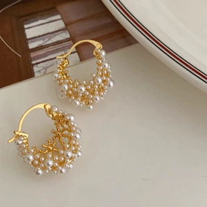 Close-up of elegant gold pearl cluster hoop earrings on a minimalist white ceramic plate