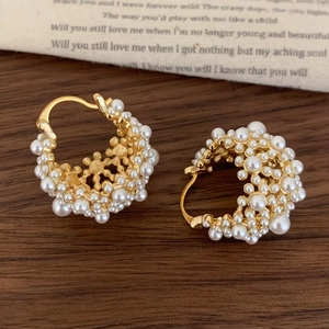 Détail de boucles d'oreilles créoles dorées avec perles blanches sur tissu vintage