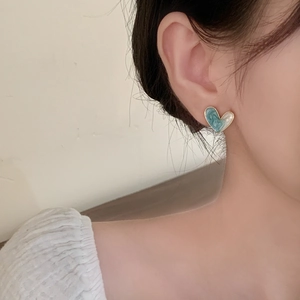 Blue marble texture and white heart stud earrings with gold trim on model ear