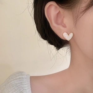 Close-up of heart-shaped earring with white shell inlay and gold metal trim on model