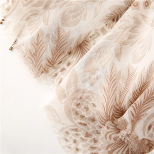Macro view of beige floral scarf featuring fringe edges and lightweight translucent fabric