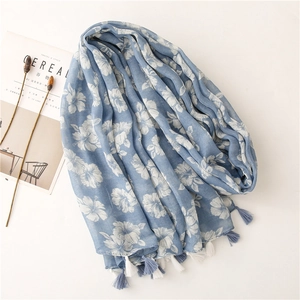 Light blue cotton linen scarf with white floral patterns and fringe tassels on white background