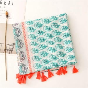 Detail of floral voile scarf featuring orange tassels and tropical print on white fabric