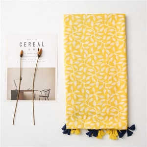 Detail of lemon yellow scarf with white leaf patterns and bi-color tassels on white surface