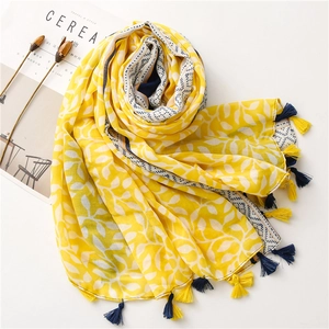 Detail of yellow and white leaf print scarf with colorful tassel edges and soft texture