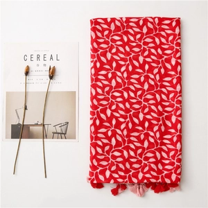 Detail of red scarf featuring white leaf prints and fringe tassels on a clean surface