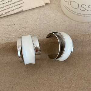 Macro view of C-shaped silver alloy earrings with white enamel wavy layered details