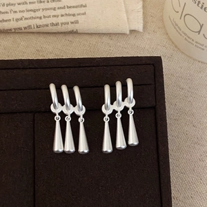 Close-up of matte silver water drop tassel earrings on a premium display stand