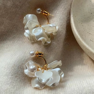 Close-up of elegant petal earrings with white pearls on a soft beige knit fabric