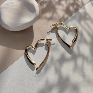 Détail de boucles d'oreilles cœur dorées aux lignes irrégulières et ombres naturelles