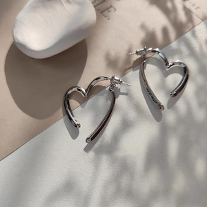 Détail de boucles d'oreilles cœur en argent poli avec ombres de feuilles sur fond minimaliste