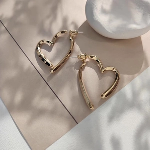 Vue détaillée de boucles d'oreilles cœur dorées avec ombre de feuilles sur fond beige