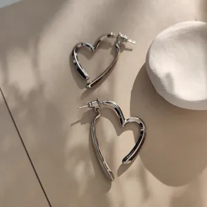 Vue détaillée de boucles d'oreilles cœur en argent poli au design ajouré sur fond beige
