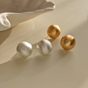 Detailed view of matte gold and brushed silver round stud earrings on a beige background
