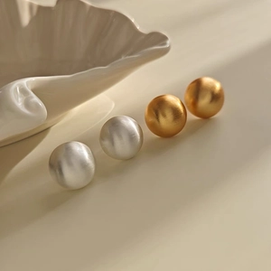 Detail of round brushed metal stud earrings in gold and silver finish with matte texture