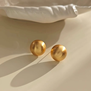 Close-up of golden round stud earrings featuring a refined brushed matte metal texture