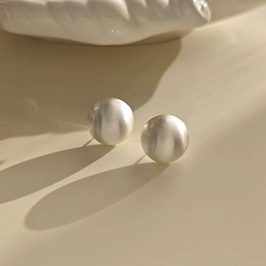 Macro detail of round brushed silver earrings featuring textured finish and artistic shadows