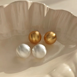 Detail of round brushed metal stud earrings in gold and silver on a ceramic tray