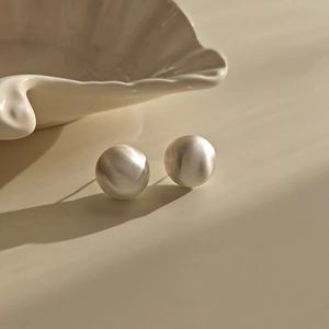 Detail of minimalist brushed silver sphere studs on a warm beige background