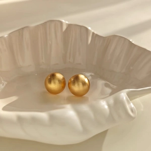Detailed view of matte brushed gold spherical stud earrings on a ceramic shell tray