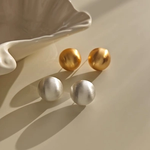 Detail view of round brushed metal stud earrings in gold and silver finishes