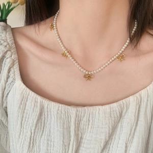 Collier élégant en perles avec pendentifs nœuds dorés porté par un mannequin femme