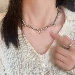 Détail du collier de perles et de la bague avec nœud papillon sur chaîne minimaliste