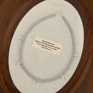 Détail du collier de perles avec cinq pendentifs nœuds argentés posé sur un plateau