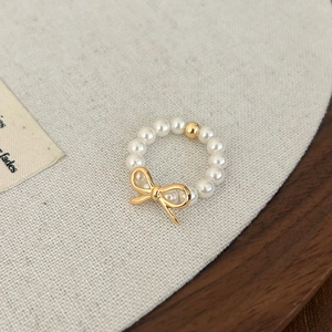 Vue détaillée d'une bague en perles avec nœud doré sur un fond en tissu texturé