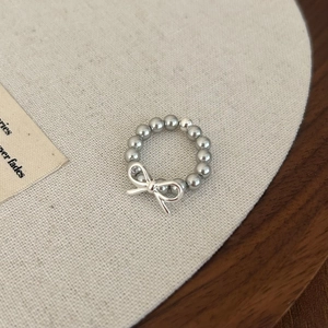 Détail d'une bague en perles argentées avec un pendentif nœud sur un support textile