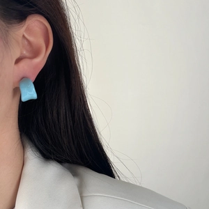 Close-up of light blue irregular resin stud earring worn on model for summer look
