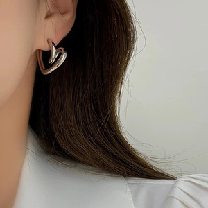 Close-up of minimalist silver heart stud earrings worn by a model on white background