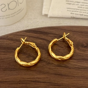 Detailed shot of gold twisted rope hoop earrings with matte finish on a wooden tray