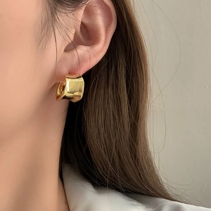 Close-up of a model wearing a thick, polished gold C-shape earring with a glossy finish