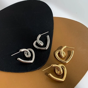 Flat lay of twisted heart stud earrings in gold and silver finish on leather textured base