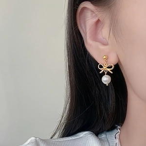 Elegant gold bow earrings with white round pearls worn by a model in a close-up view