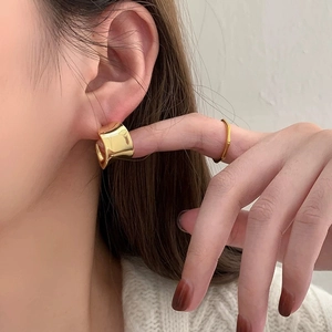 Close-up of modern gold-tone twisted wide-surface hoop earrings worn by a model