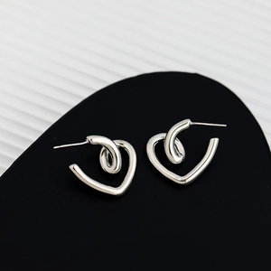 Macro shot of silver twisted heart-shaped stud earrings on a sleek black display stand