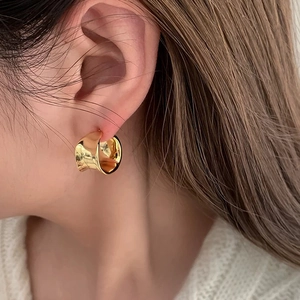 Close-up of a model wearing a thick golden C-shaped earring with polished mirror finish