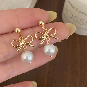 Detail of elegant gold bow earrings with hanging pearls held by hand for scale