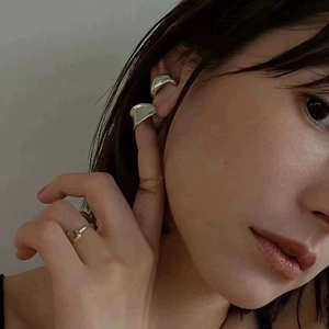 Detail showing irregular silver C-shaped stud earrings and square stone ring on model