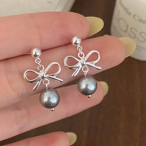 Detail of silver bow earrings with dark grey pearls held by hand for scale