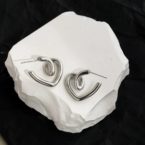 Close-up of silver heart-shaped knot earrings on a white stone background