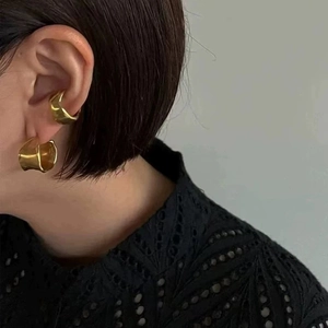 Detail view of gold irregular C-shape ear cuff and earring set on model's ear