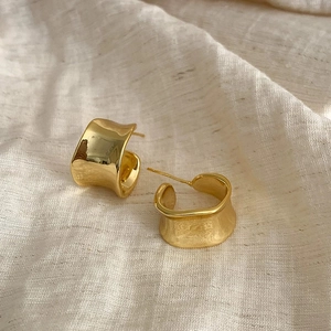 Detailed view of gold C-shaped irregular earrings with wavy texture on linen