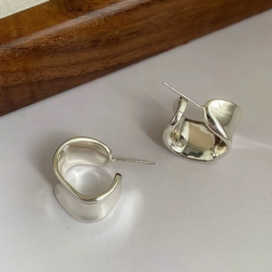 Close-up of irregular C-shaped wide earrings with polished liquid metal finish