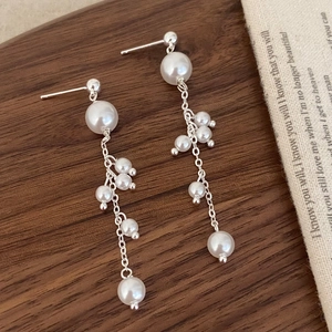 Detail of silver long tassel earrings with lustrous pearls on a wooden surface