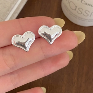 Close-up of minimalist heart stud earrings in polished silver finish held by hand